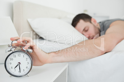 Sleeping young man being awakened by an alarm clock