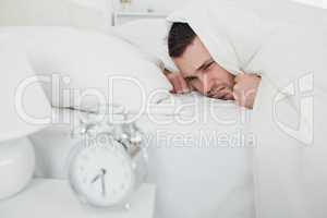 Man covering his ears while his alarm clock is ringing