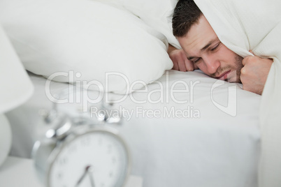 Young man covering his ears while his alarm clock is ringing