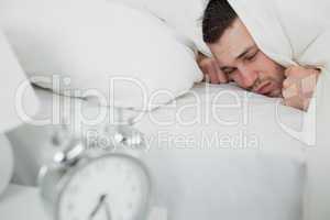 Young man covering his ears while his alarm clock is ringing