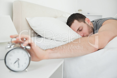 Sleeping handsome man being awakened by an alarm clock
