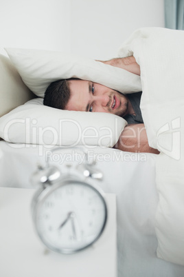 Portrait of a tired young man covering his ears while his alarm