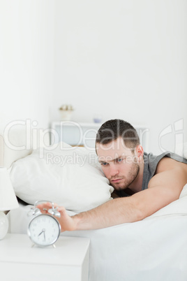 Portrait of a unhappy man being awakened by an alarm clock