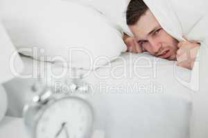 Annoyed man covering his ears while his alarm clock is ringing