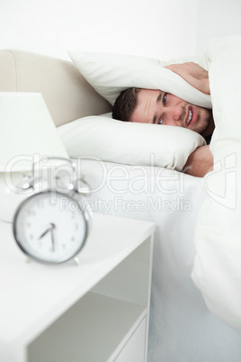 Portrait of a unhappy man covering his ears with a pillow