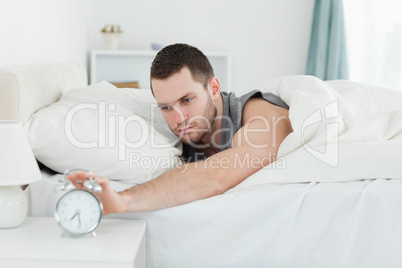 Tired man being awakened by an alarm clock