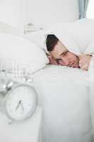 Portrait of a young man covering his ears while his alarm clock
