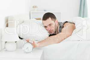 Exhausted man switching off his alarm clock