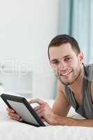 Portrait of an attractive man using a tablet computer while lyin