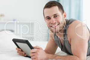 Happy man using a tablet computer while lying on his belly