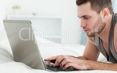 Serious man using a laptop while lying on his belly