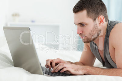 Focused man using a laptop while lying on his belly