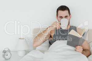 Man reading a novel while holding a cup of coffee