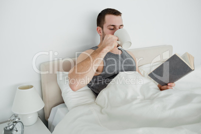 Smiling man reading a novel while drinking a coffee