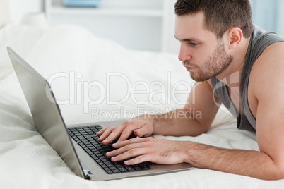 Young man using a laptop while lying on his belly