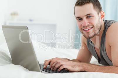 Happy man using a laptop while lying on his belly