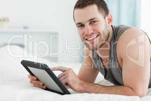 Smiling man using a tablet computer while lying on his belly