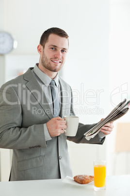 Portrait of a smiling businessman having breakfast while reading