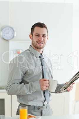 Portrait of a smiling businessman reading the news while having