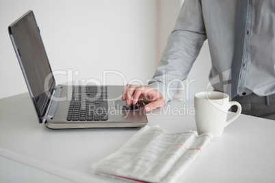Businessman using a laptop with a cup of tea and a newspaper