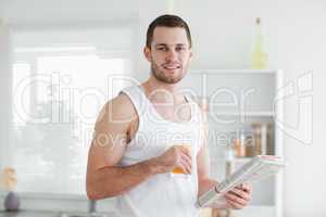Smiling man drinking orange juice while reading the news