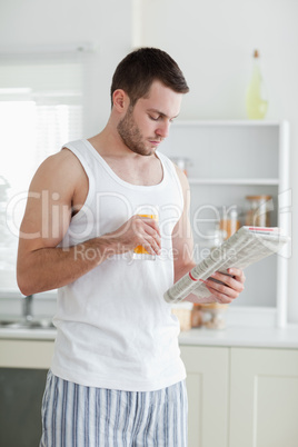 Portrait of a handsome man drinking orange juice while reading t