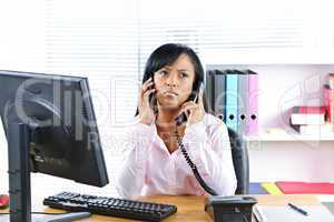 Black businesswoman using two phones at desk