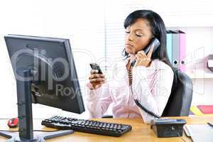 Black businesswoman using two phones at desk