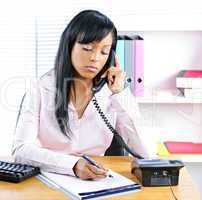 Serious black businesswoman on phone at desk