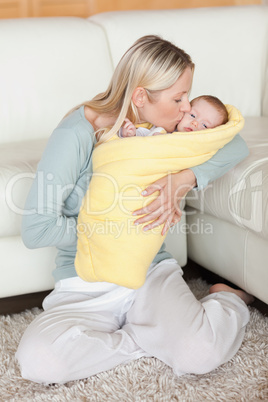 Mom kissing her baby that is wrapped into a cover