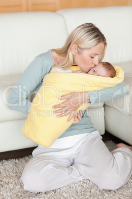 Affectionate mom kissing her baby that is wrapped into a cover