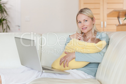 Mother with laptop on the sofa holding her baby