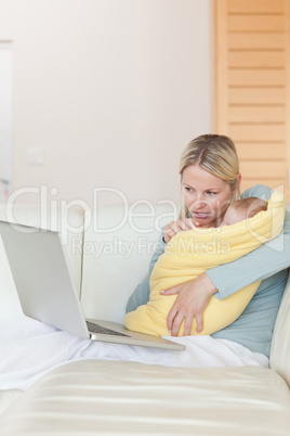 Mother with notebook on the couch holding her baby