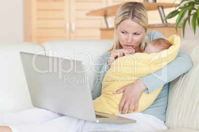 Mother holding her baby while looking at her laptop