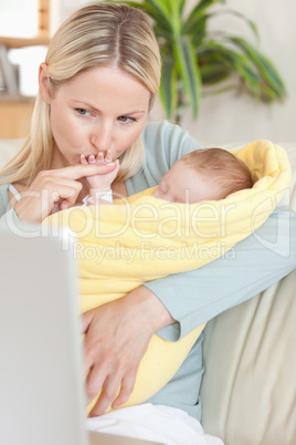 Mother kissing her baby's hand while looking at the laptop
