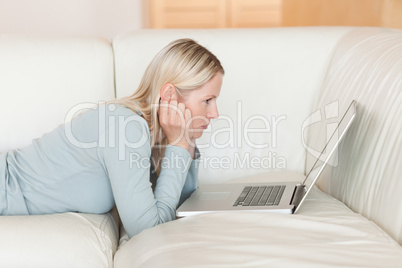 Side view of woman with laptop lying on the sofa
