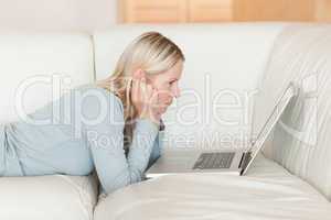 Side view of woman with laptop lying on the sofa