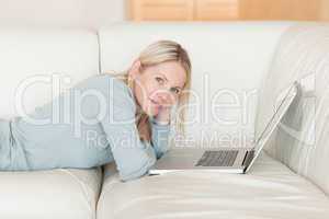 Side view of woman with laptop lying on the couch