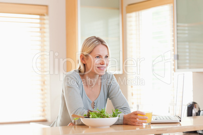 Female with salad and laptop in the kitchen having a glass of or