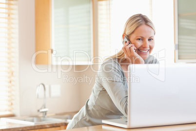 Smiling woman on the phone looking at her laptop