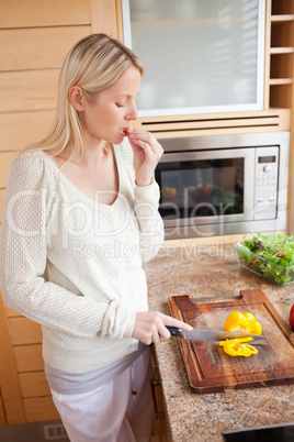 Side view of woman nibbling while cutting bell pepper