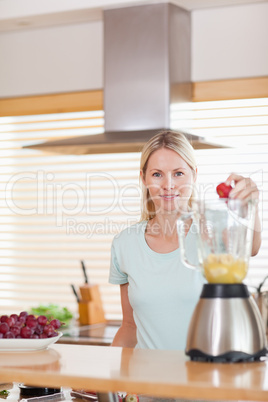 Woman putting strawberry into the blender