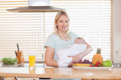 Woman standing in the kitchen while holding her baby