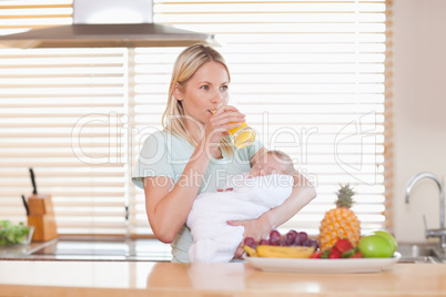 Woman taking a sip of juice while holding her baby