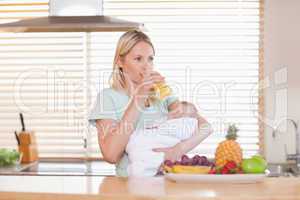 Woman taking a sip of juice while holding her baby