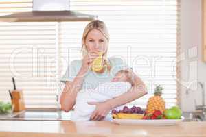 Woman drinking juice while holding her baby