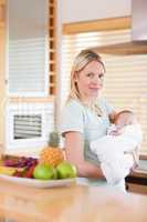 Side view of woman standing in the kitchen with her baby on her