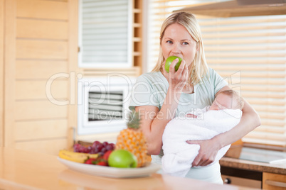 Woman with baby on her arms eating an apple