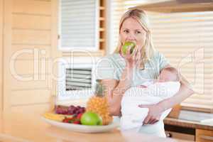 Woman with baby on her arms eating an apple