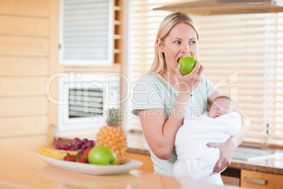 Woman biting into apple with baby on her arms